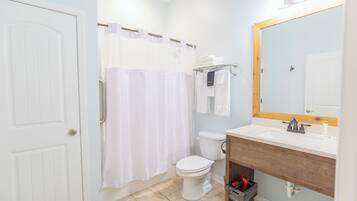Un baño con inodoro blanco, cortina de ducha, lavabo con tocador de madera y espejo con marco de madera.