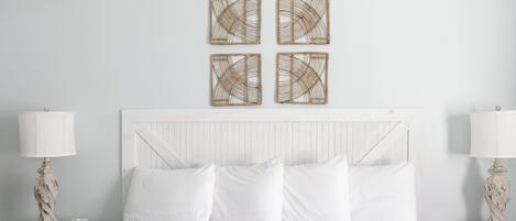 A neatly made bed with white linens, two bedside tables with lamps, and four wall-mounted decorative items.