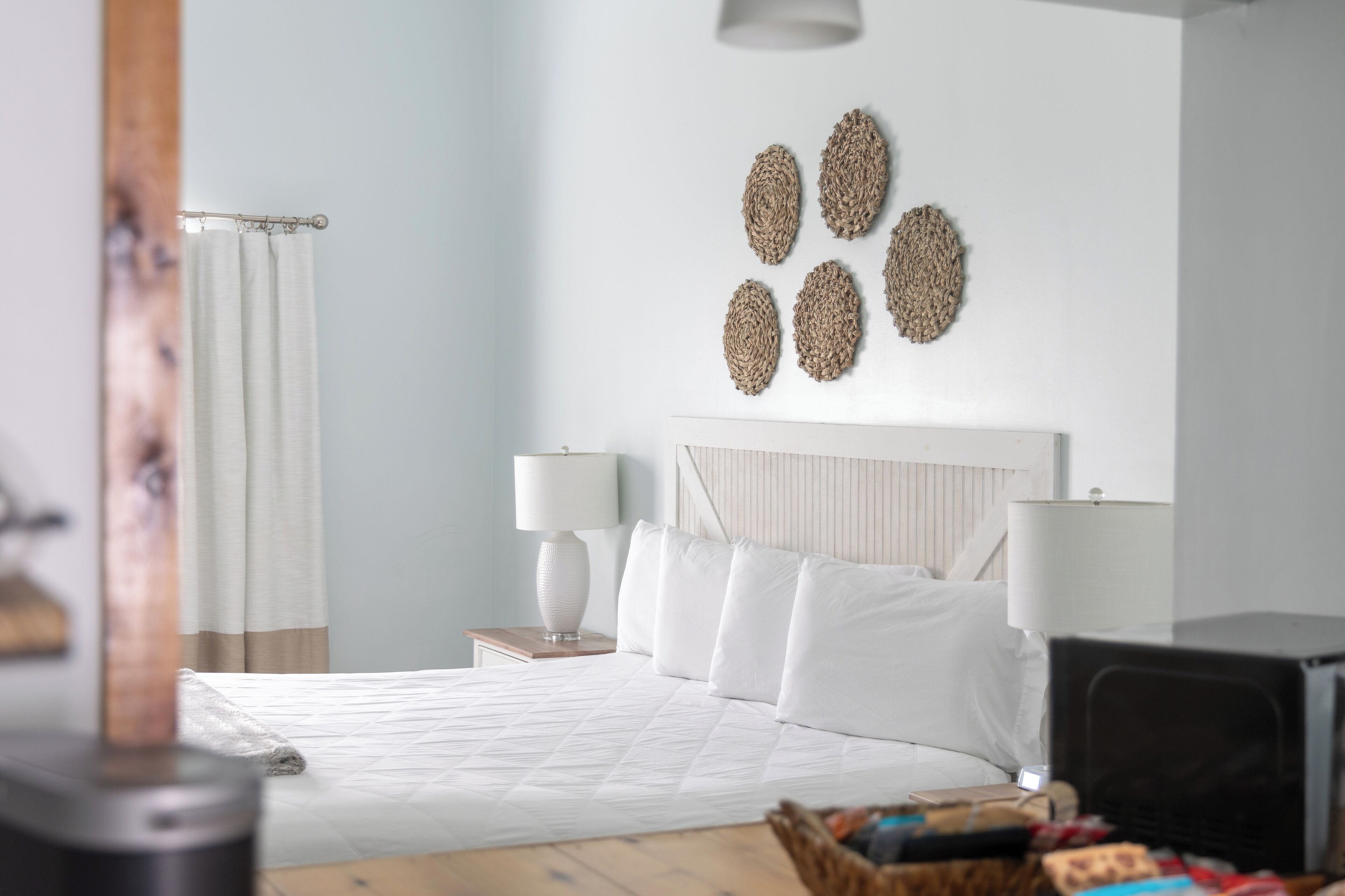 A neatly arranged bedroom with a bed, bedside lamps, a headboard, and a wall-mounted decorative piece.