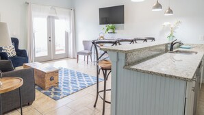 Eine moderne Küche mit Kochinsel, Essbereich mit Stühlen, einem an der Wand montierten Fernseher und einem Deckenventilator.
