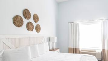 Una cama bien hecha con sábanas blancas, una lámpara de noche y una ventana con cortinas.