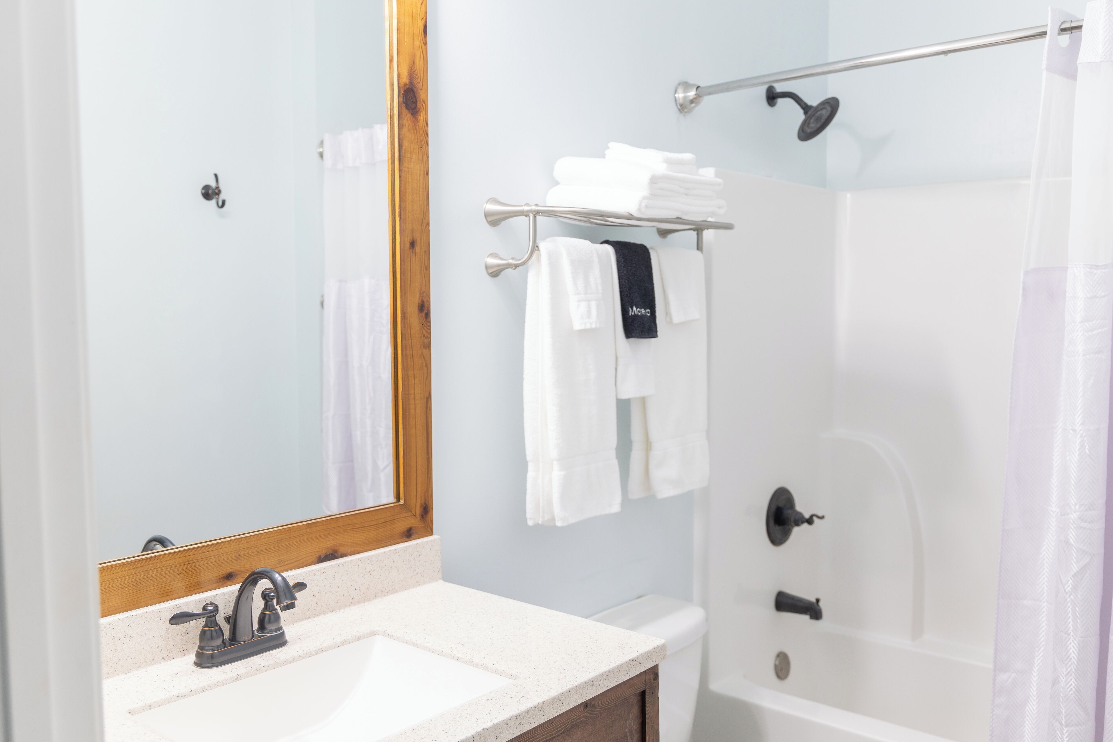 Un bagno con lavandino, specchio, porta asciugamani e doccia.