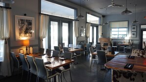 Ein moderner Essbereich mit mehreren Tischen und Stühlen, großen Fenstern mit Vorhängen und Pendelleuchten.