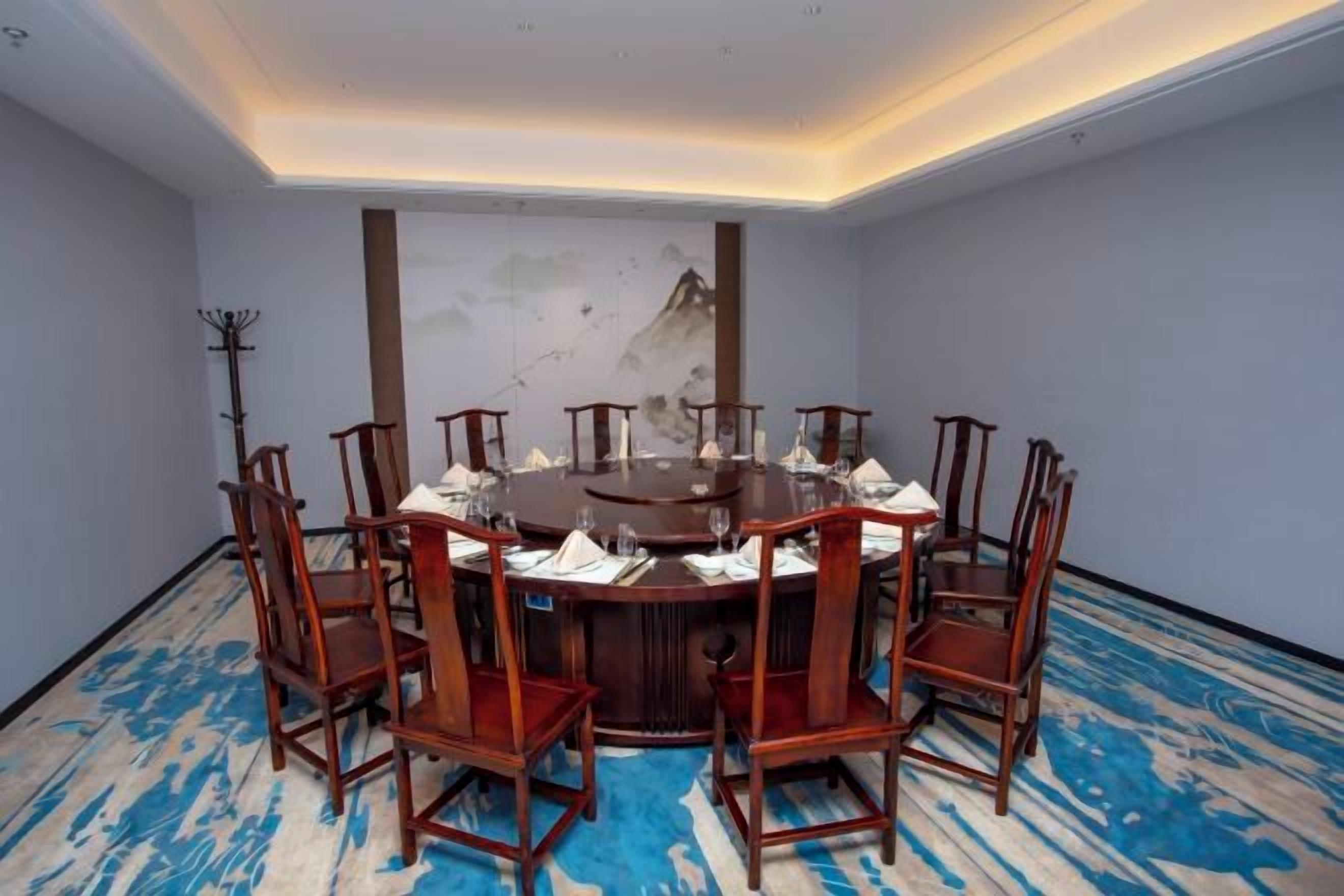 A conference room with a round table, eight chairs, and a painting on the wall.