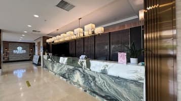 A hotel reception area with a marble counter, modern lighting fixtures, and a digital display in the background.
