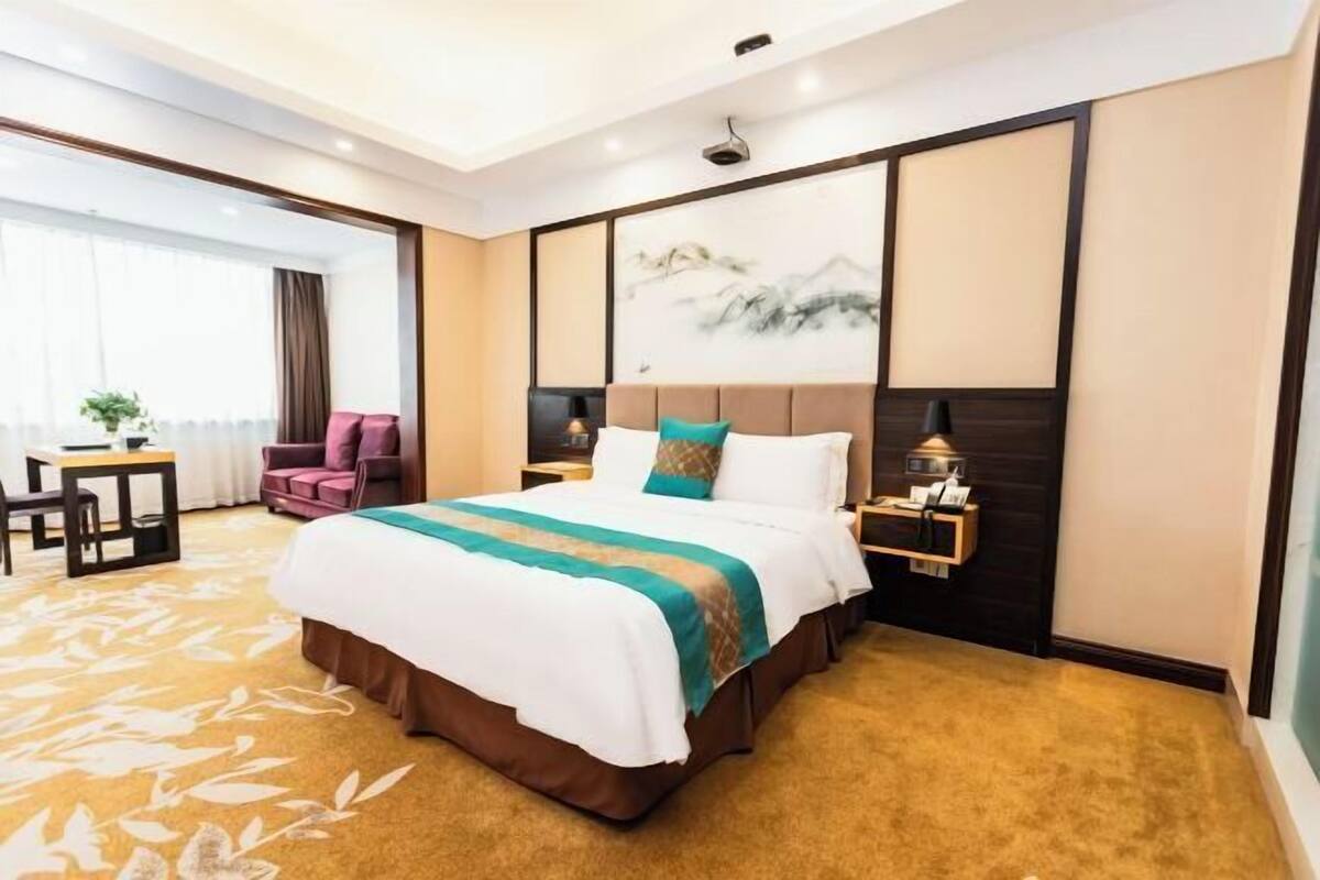 A hotel room with a large bed, a desk, a chair, and a window with curtains.