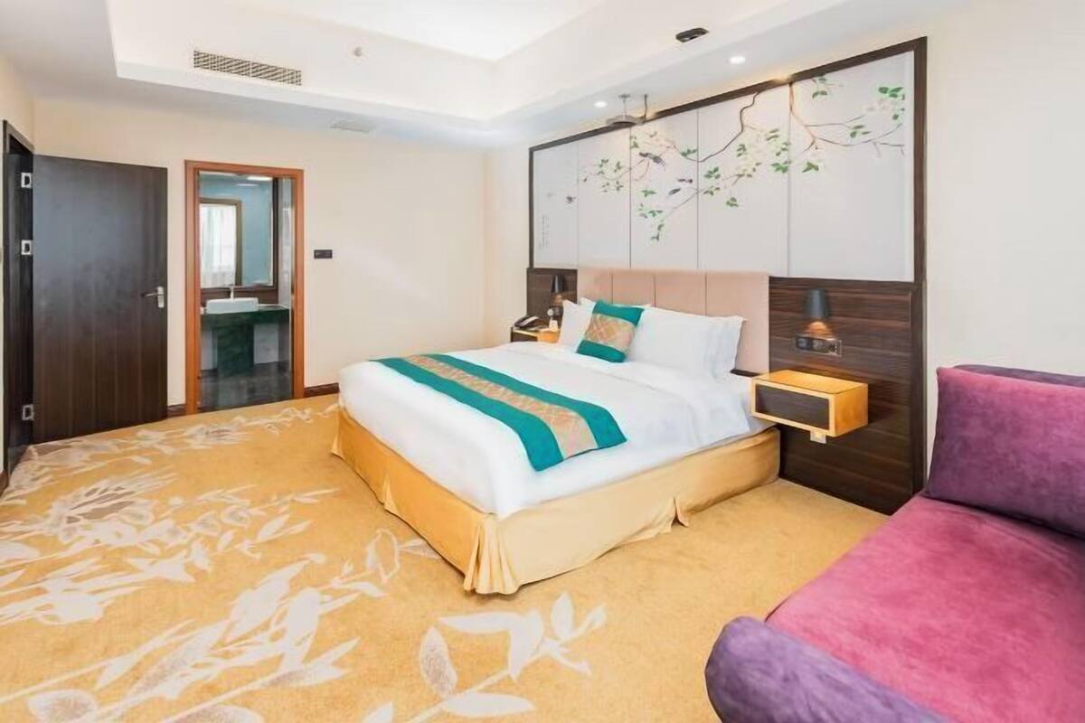 A hotel room with a bed, bedside table, nightstand, and a large window.