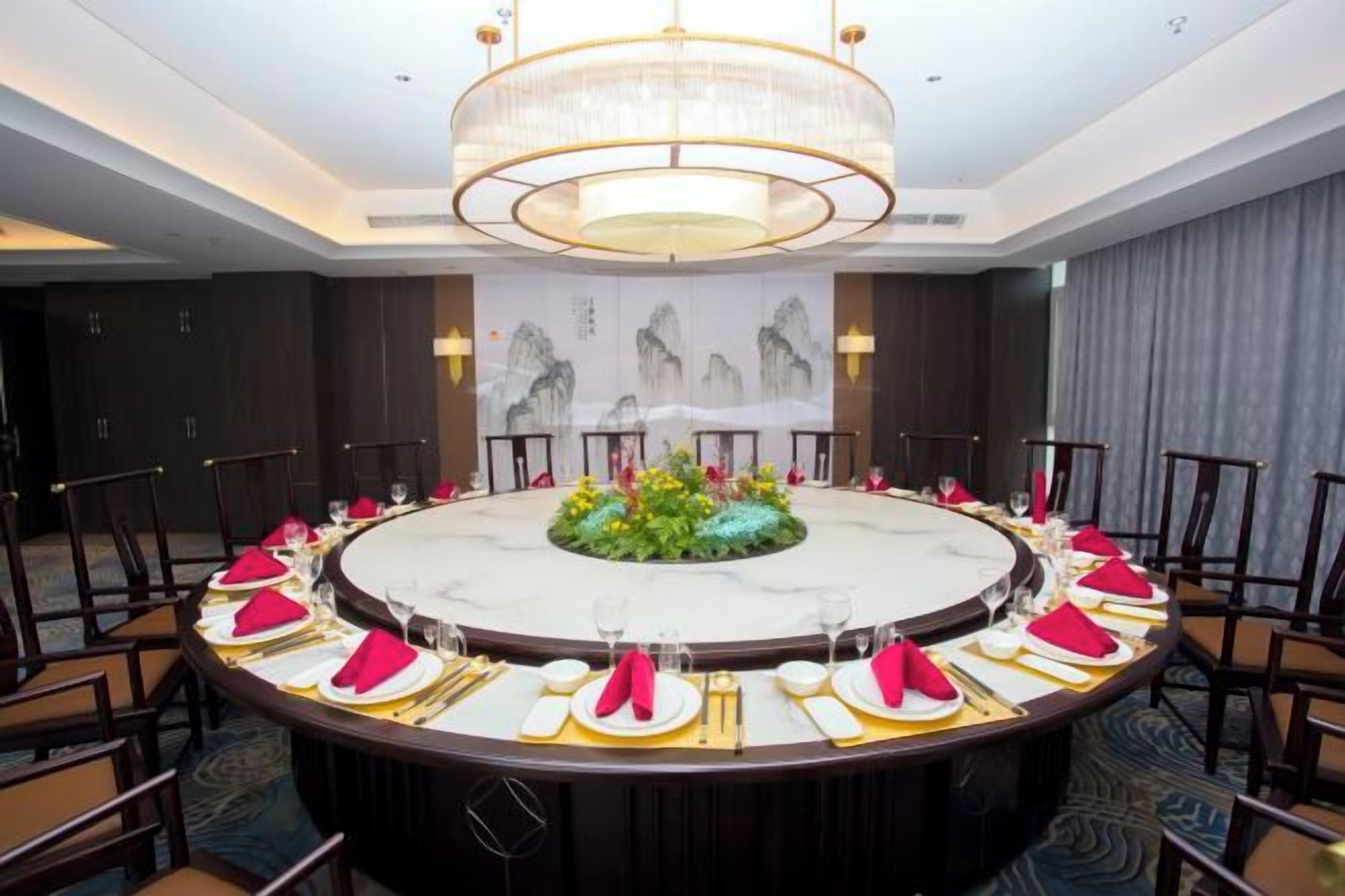 A round table set for a meeting with a chandelier above, surrounded by chairs, in a room with a large painting on the wall.