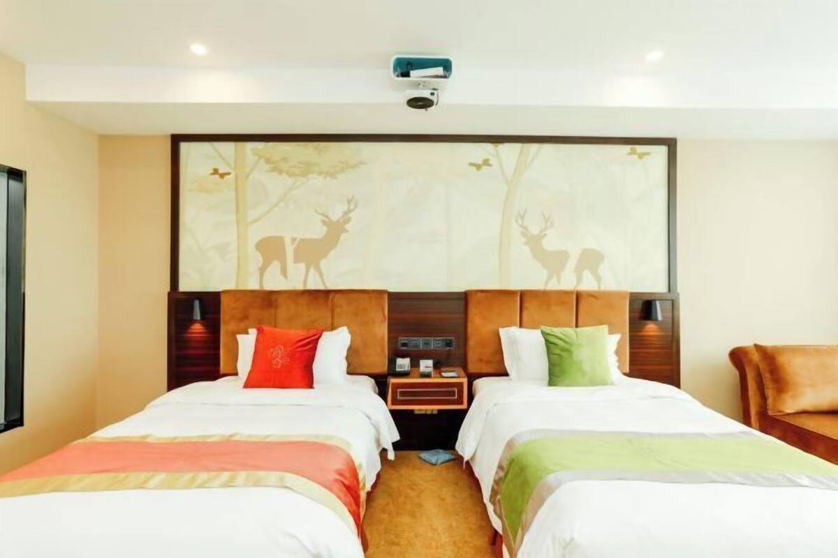 A hotel room with two beds, a headboard with a deer mural, a nightstand, and a camera on the ceiling.