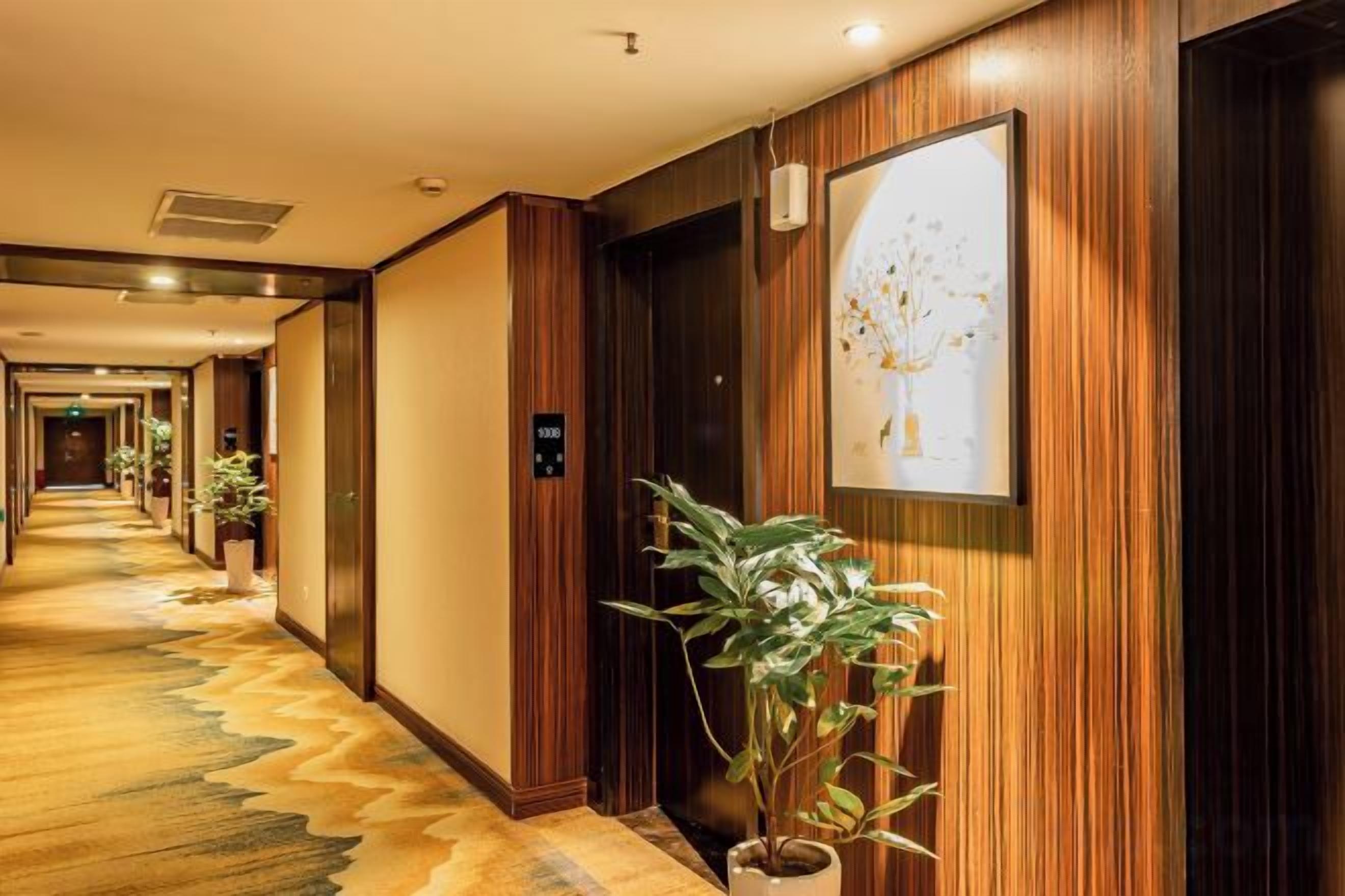 Een hotelgang met houten lambrisering, plantenbakken en een kunstwerk in een lijst aan de muur.