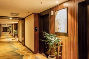 Un pasillo de hotel con paneles de madera, plantas en macetas y una obra de arte enmarcada en la pared.
