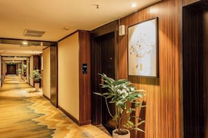 Un pasillo de hotel con paneles de madera, plantas en macetas y una obra de arte enmarcada en la pared.