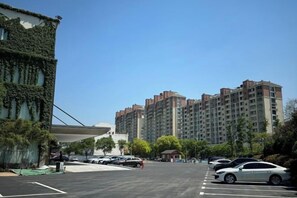 Un estacionamiento con varios autos, un edificio con muros cubiertos de hiedra y edificios residenciales altos al fondo.