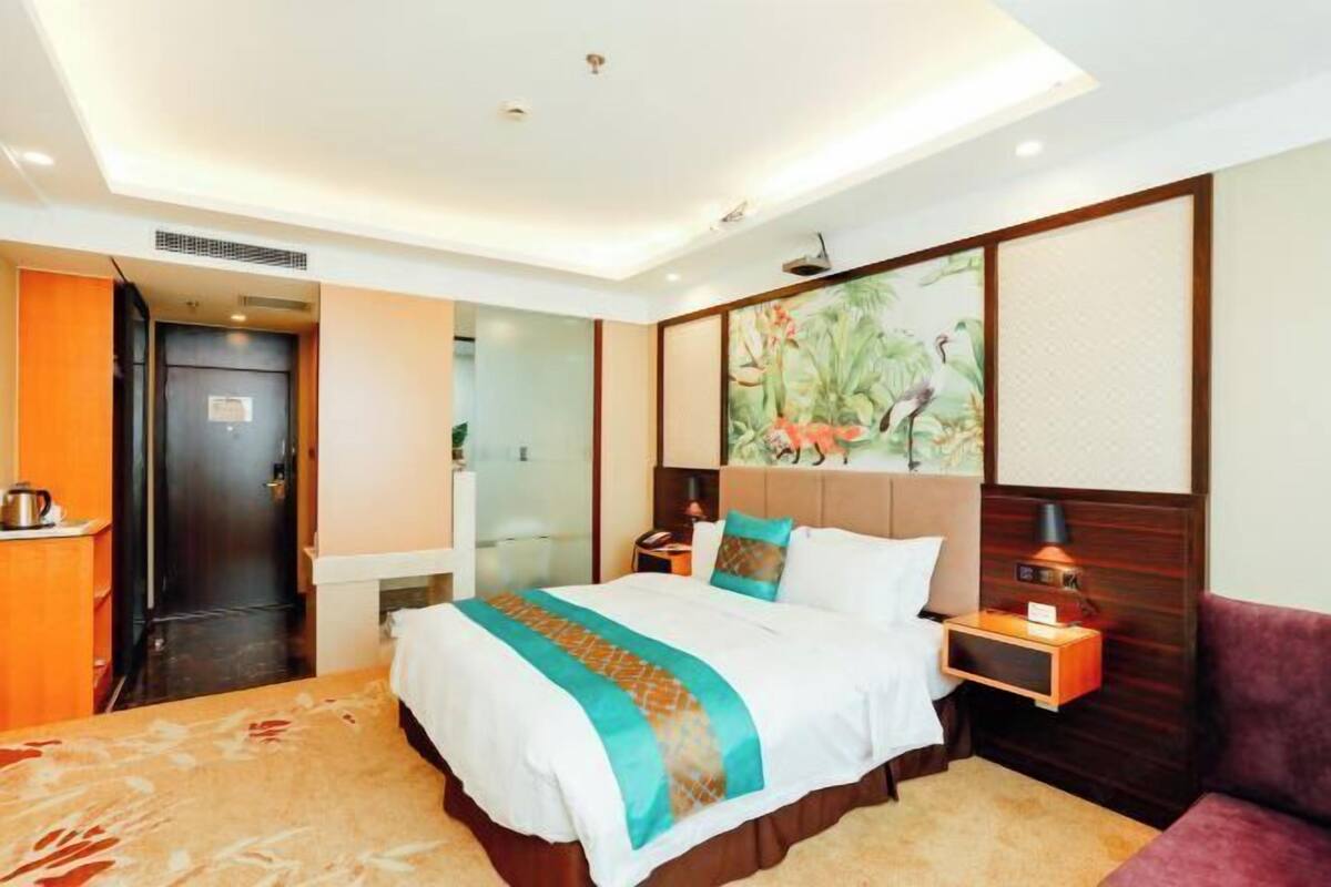 A hotel room with a bed, a nightstand, a lamp, a painting, and a door.