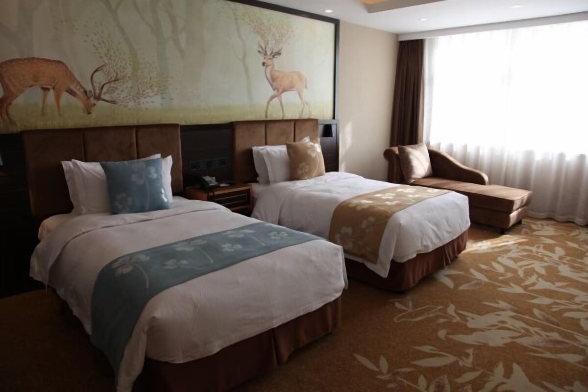 Ein Hotelzimmer mit zwei Betten, einem Sofa, einem großen Hirschgemälde und Blick ins Freie.