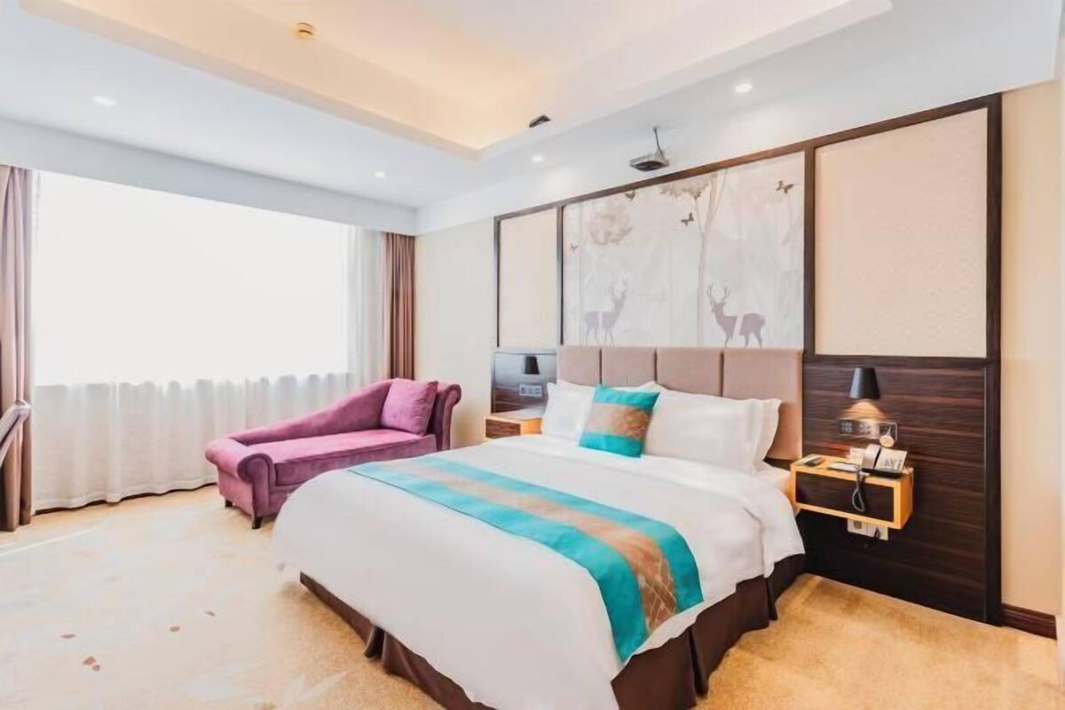 A hotel room with a large bed, a nightstand, a lamp, a window with curtains, and a wall with a deer mural.