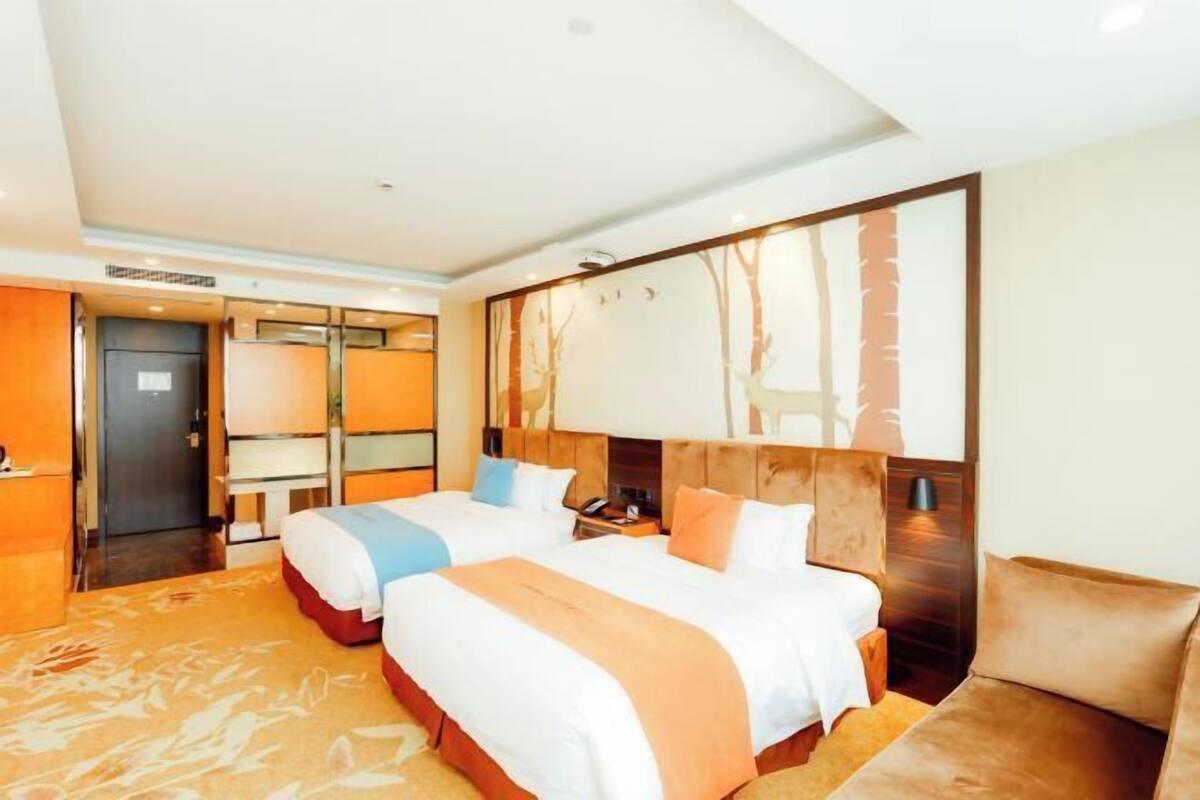 A hotel room with two beds, a sofa, a large mirror, and a door leading to a bathroom.