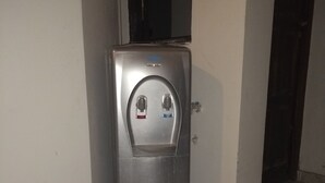 A water dispenser in a corner of a room with tiled flooring.