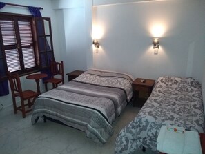 Un dormitorio con una cama, dos mesitas de noche, una silla, una pequeña mesa y una ventana con persianas.