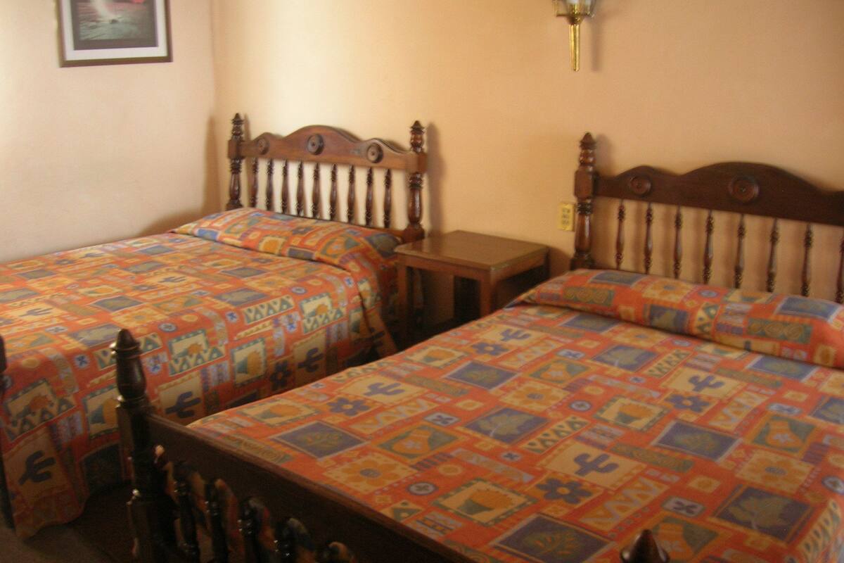A room with two wooden beds, each with a colorful quilt. There is a small wooden table between the beds.