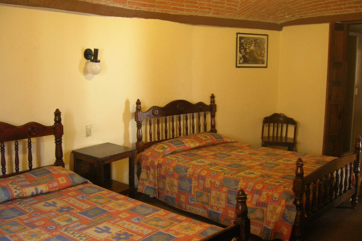 A room with two wooden beds, a small table, and a chair.