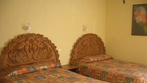 Twee houten bedden met gesneden hoofdeinden, een bloemschilderij aan de muur en een bed met een patroon.