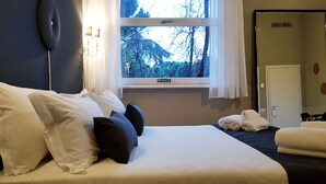 A hotel room with a bed, pillows, a window with a view of trees, a door, and a mirror. - Villa Gotti Charming Rooms (Bologna)