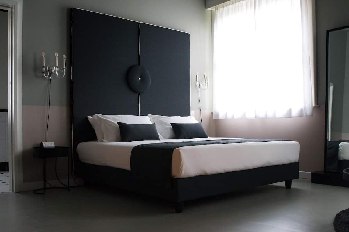 A modern bedroom with a large bed, bedside tables, a mirror, and a view of the outside.