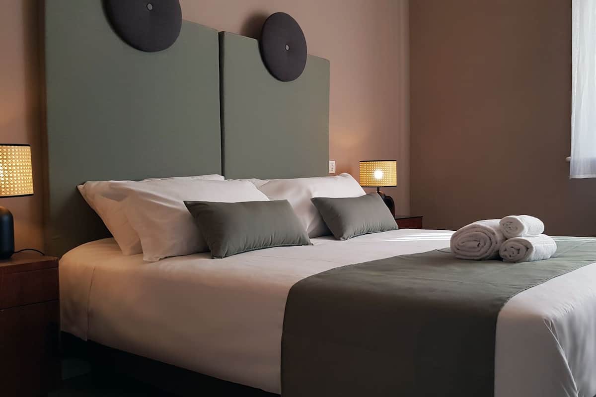 A neatly made bed with pillows and a rolled towel, a bedside lamp, and a radiator.