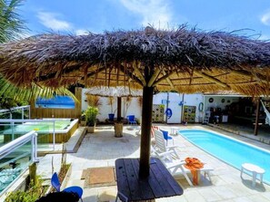 Een zwembadgedeelte met een rieten parasol, ligbedden en een jacuzzi.
