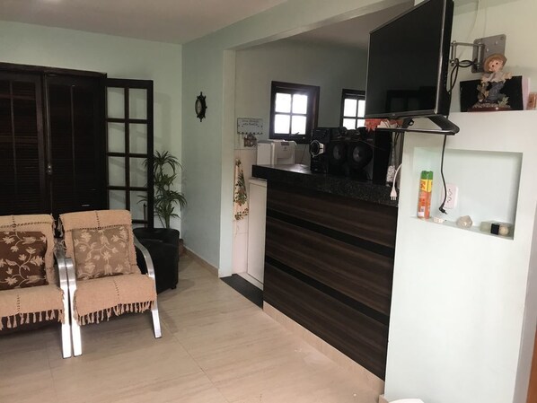 A living room with a sofa, a television, and a kitchen area with a counter and appliances.