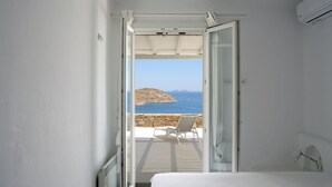 Un dormitorio con cama, una silla y vista al mar a través de una puerta abierta.