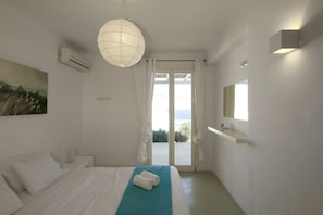 A bedroom with a bed, a hanging light fixture, a window with curtains, and a view of the outdoors.