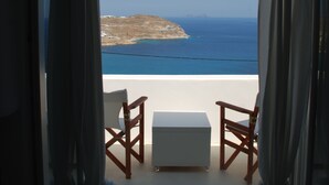 Habitación con vista a la playa y al mar. Hay dos sillas de madera y una pequeña mesa blanca.