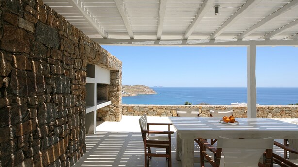 Un espacio de estar al aire libre cubierto, con paredes de piedra y vista al mar.
