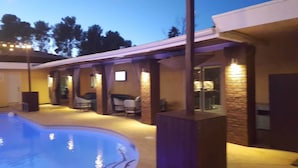 A modern outdoor pool area with a curved pool, stone pillars, and a covered seating area with chairs. - 5615 Properties (Las Vegas)