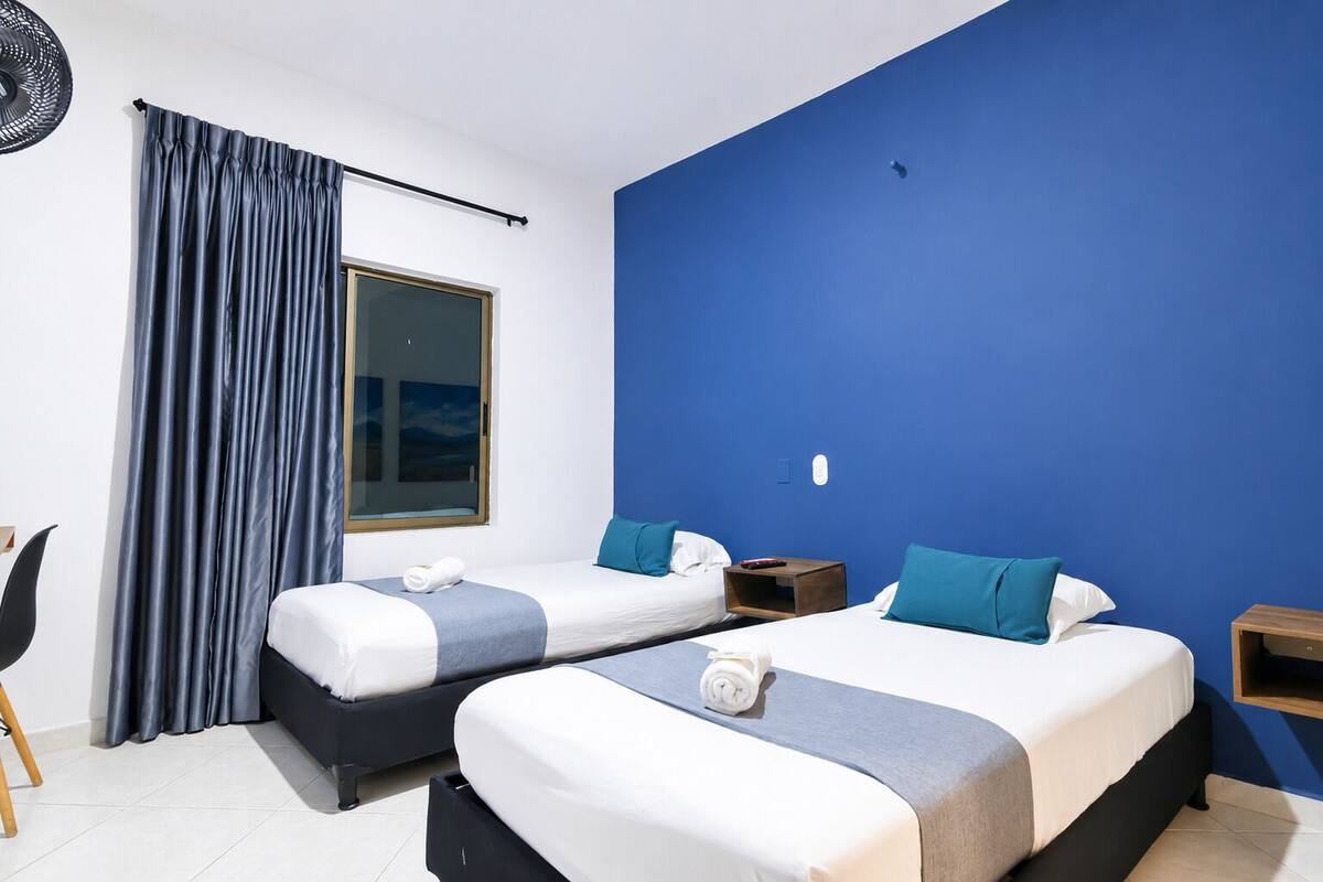 Ein Hotelzimmer mit zwei Betten, einem großen Fenster, einem Ventilator und Blick auf den Himmel.