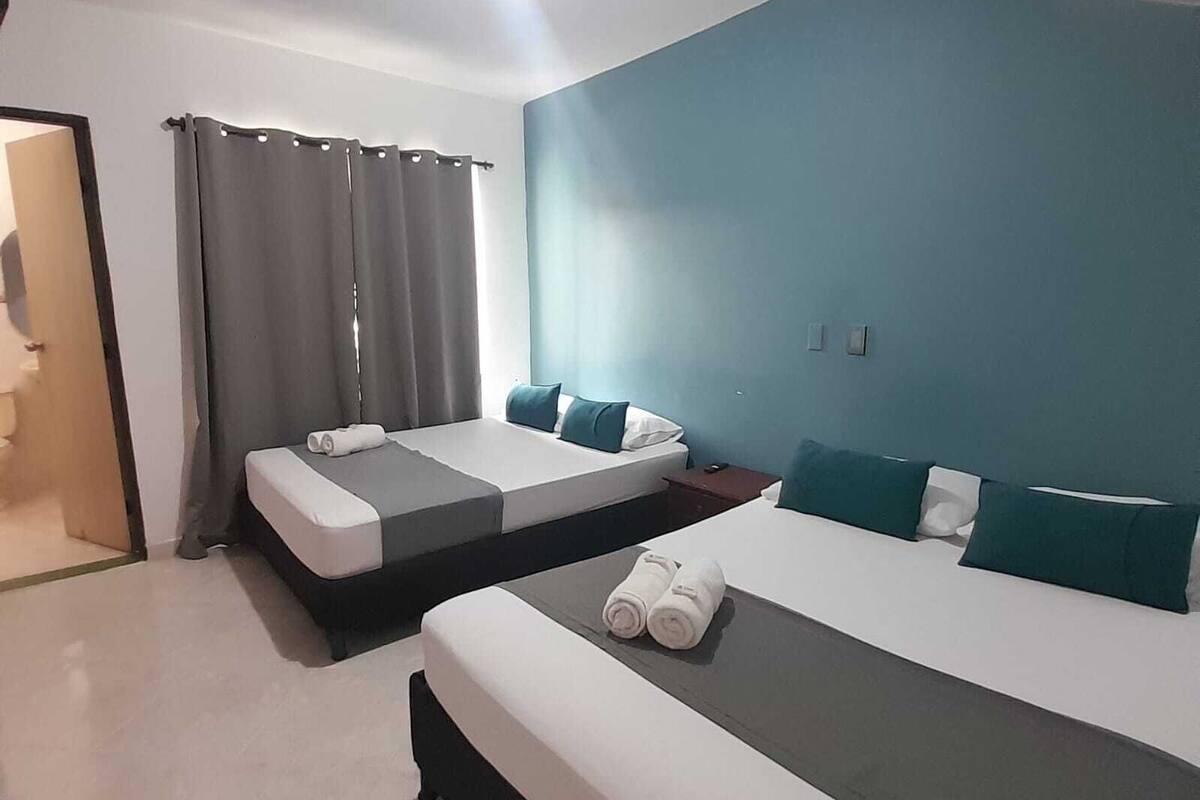 Ein Hotelzimmer mit zwei Betten, einem Deckenventilator und einer Tür zu einem anderen Raum.