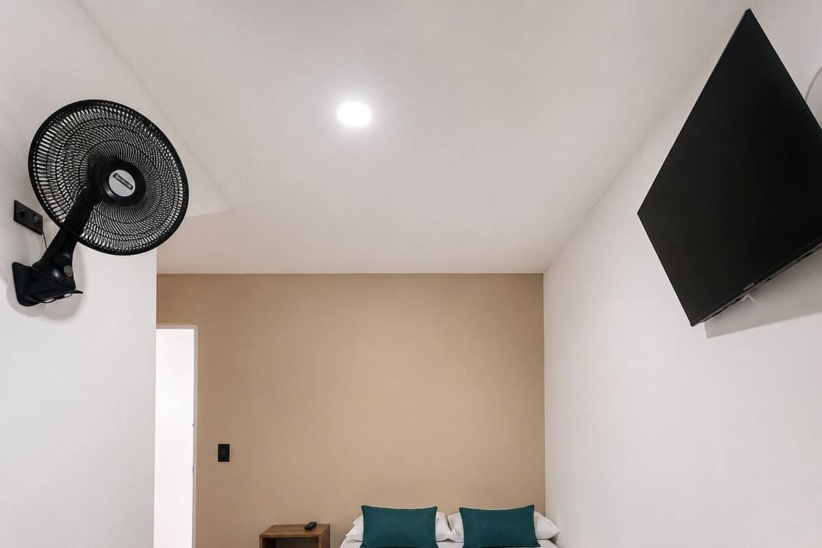 Ein Hotelzimmer mit einem Bett, einem Schreibtisch, einem Fernseher, einem Ventilator und einem Boden mit Steinmuster.