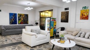 A modern living room with a grey sofa, a white armchair, a beige sofa, and a coffee table with magazines. There are abstract paintings on the walls and a refrigerator with a colorful design. - Hotel Balcones de la 70 (Medellín)