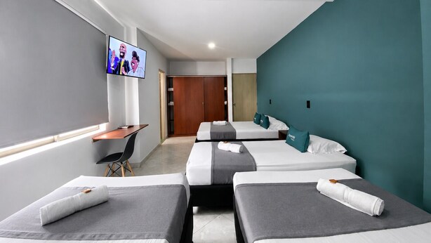 A hotel room with three beds, a desk, a TV, and a wardrobe. - Hotel Balcones de la 70 (Medellín)