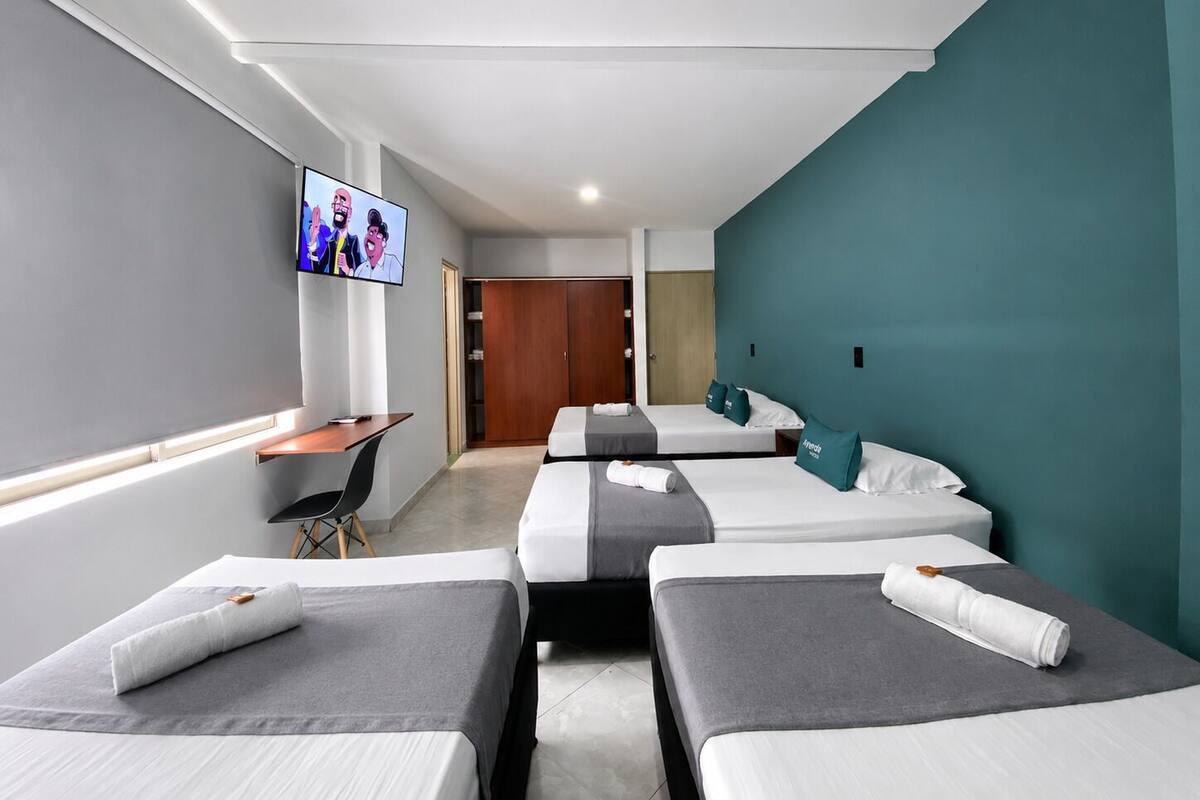 Ein Hotelzimmer mit drei Betten, einem Schreibtisch, einem Fernseher und einem Kleiderschrank.