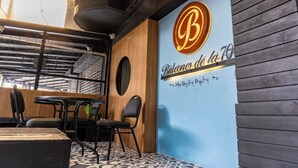 A restaurant interior with a wooden wall, a large illuminated 'B' logo, and a tiled floor. - Hotel Balcones de la 70 (Medellín)