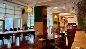 A spacious dining area with multiple tables and chairs, large windows, and hanging light fixtures. - STX Resort (Mungyeong)