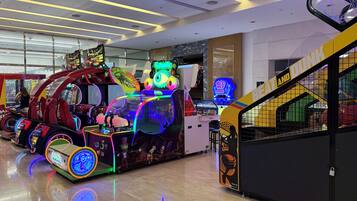 Um salão de jogos indoor com diversas máquinas de entretenimento, uma escadaria visível e um letreiro de neon.