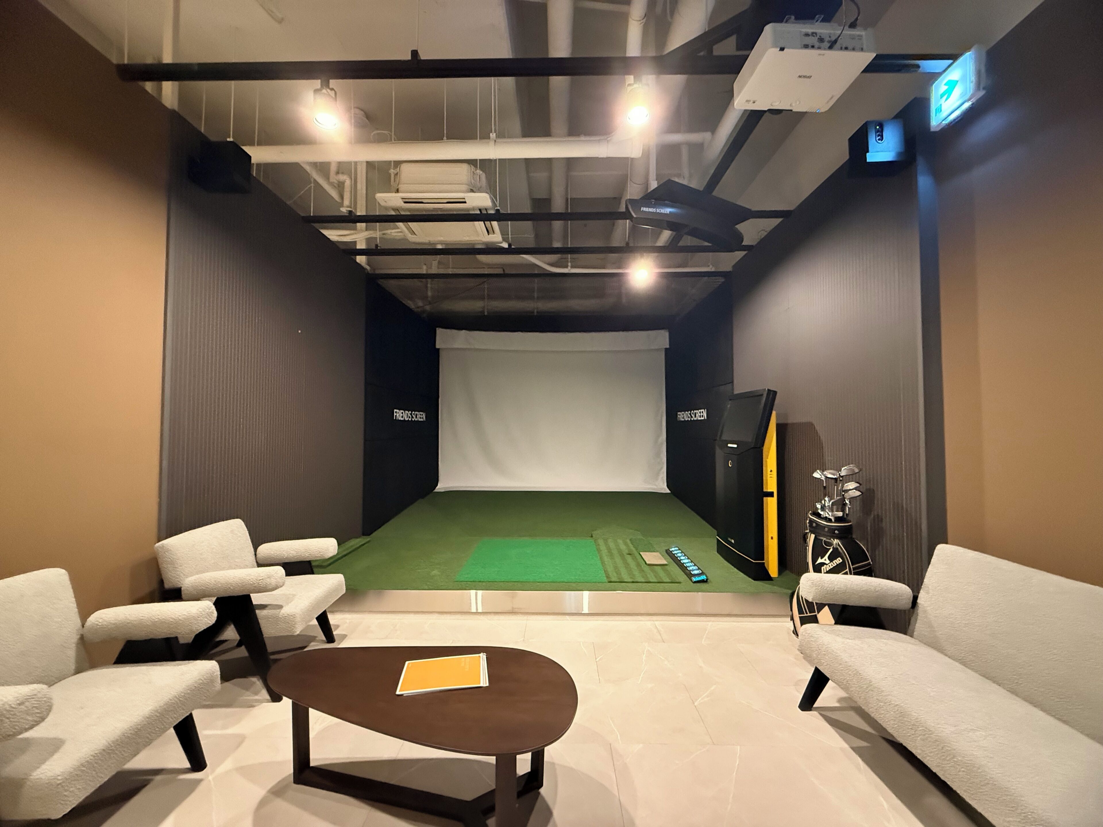 A room with a green carpet, white chairs, a brown table, a projector, and a screen.