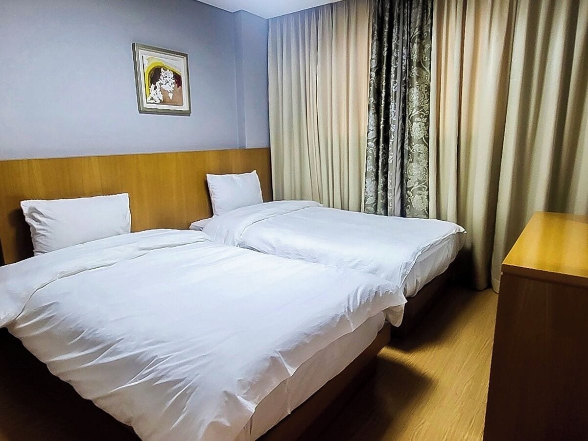 A hotel room with two beds, a wooden headboard, a bedside table, and a framed picture on the wall.