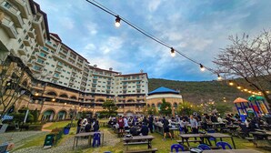 A courtyard with outdoor seating, a large building with multiple balconies, and a playground. - STX Resort (Mungyeong)
