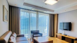A modern living room with a sofa, armchair, coffee table, TV, and large windows with curtains. - STX Resort (Mungyeong)