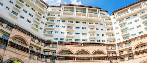 Un hotel de varios pisos con un patio central, balcones y cielo despejado.
